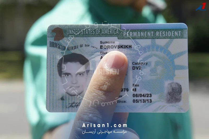 کارت اقامت دائم آمریکا (گرین کارت) که توسط یک فرد در دست گرفته شده است. اطلاعاتی مانند نام، عکس، و تاریخ صدور بر روی کارت مشخص است. در پس‌زمینه، فردی با لباس سبز رنگ دیده می‌شود. آدرس وب‌سایت Arisan1.com و نام  مؤسسه مهاجرتی آریسان در پایین تصویر قرار دارد. این کارت راهی برای شهروندی و بهره‌مندی از مزایای اقامت دائم در آمریکا است.